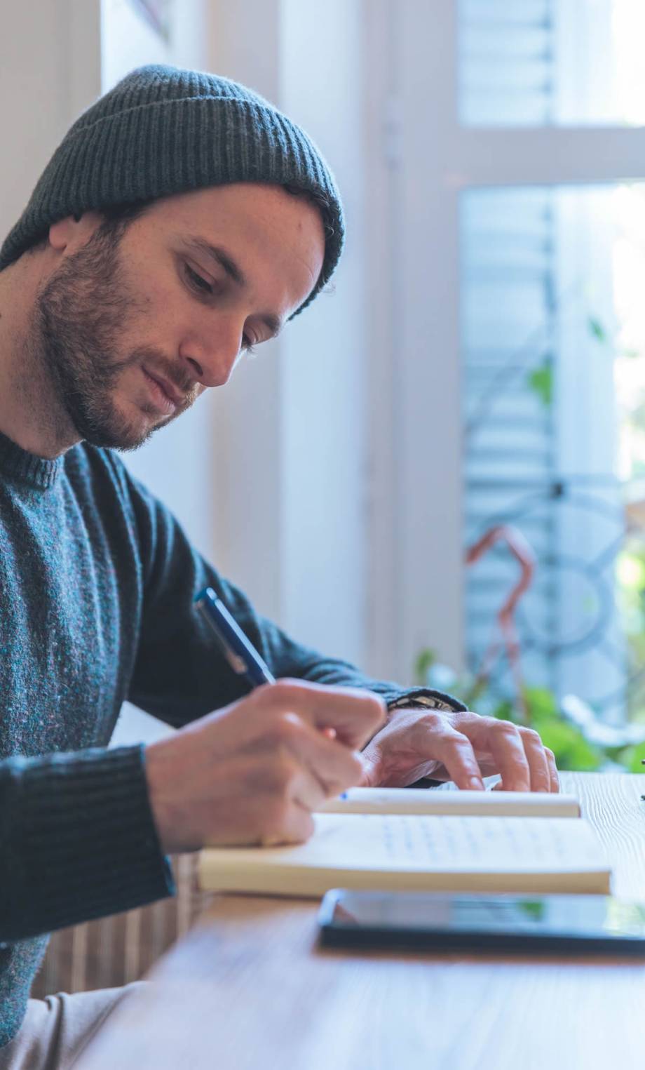 young-man-writing-in-a-notebook-near-the-window
